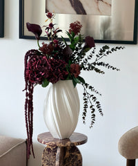 Kunstblumenstrauß Merlot Night in Bordeaux & Grün aus der Serie Bloom – auf dem Marmorsockel im Wohnzimmer