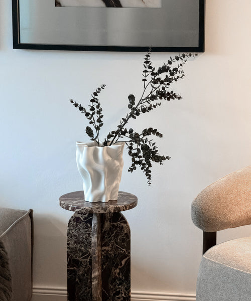 Cleo Vase mit Eukalyptuszweigen auf einer Marmorsäule im Wohnzimmer
