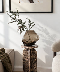 Suri Vase mit Eukalyptuszweigen auf einer Marmorsäule im Wohnzimmer